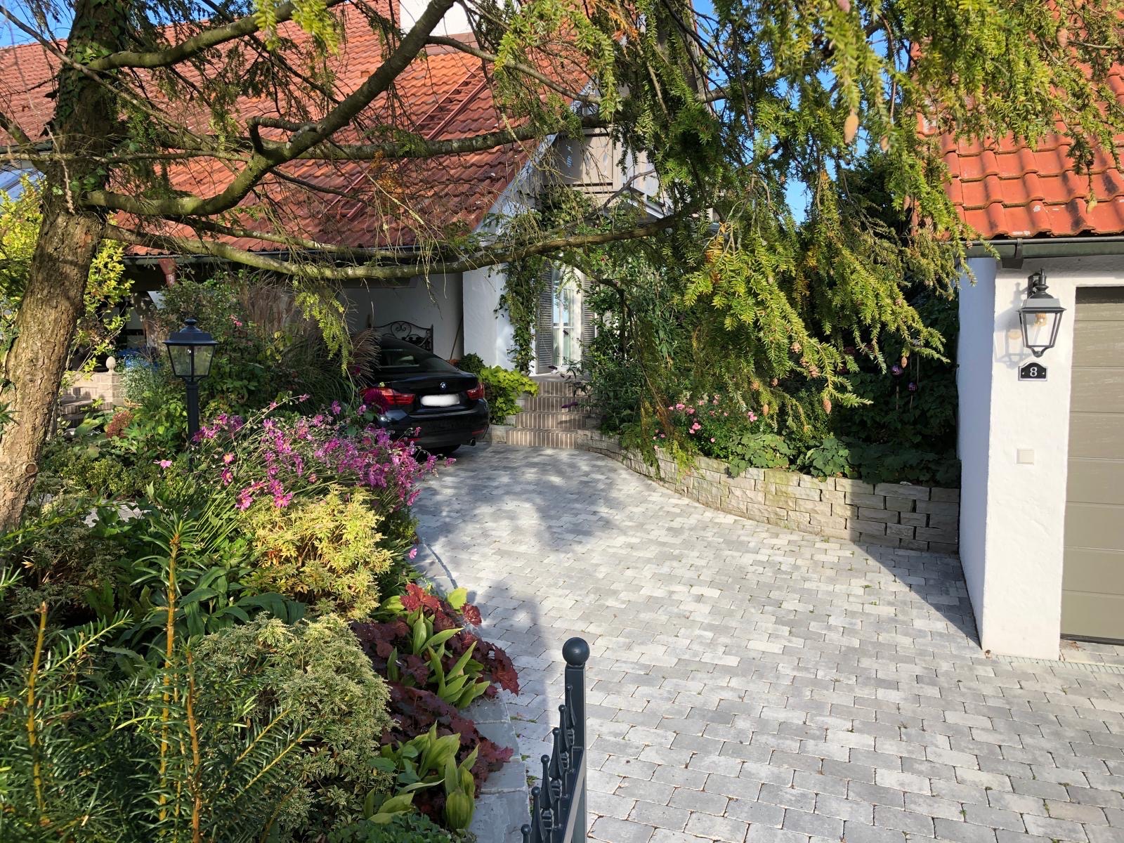 gepflasterte Einfahrt mit Blick auf Vorgarten und Haus mit ummauerten Beeten